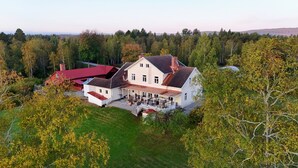 Une grande maison à deux étages, dotée d’un patio couvert et d’une dépendance adjacente avec un toit rouge.