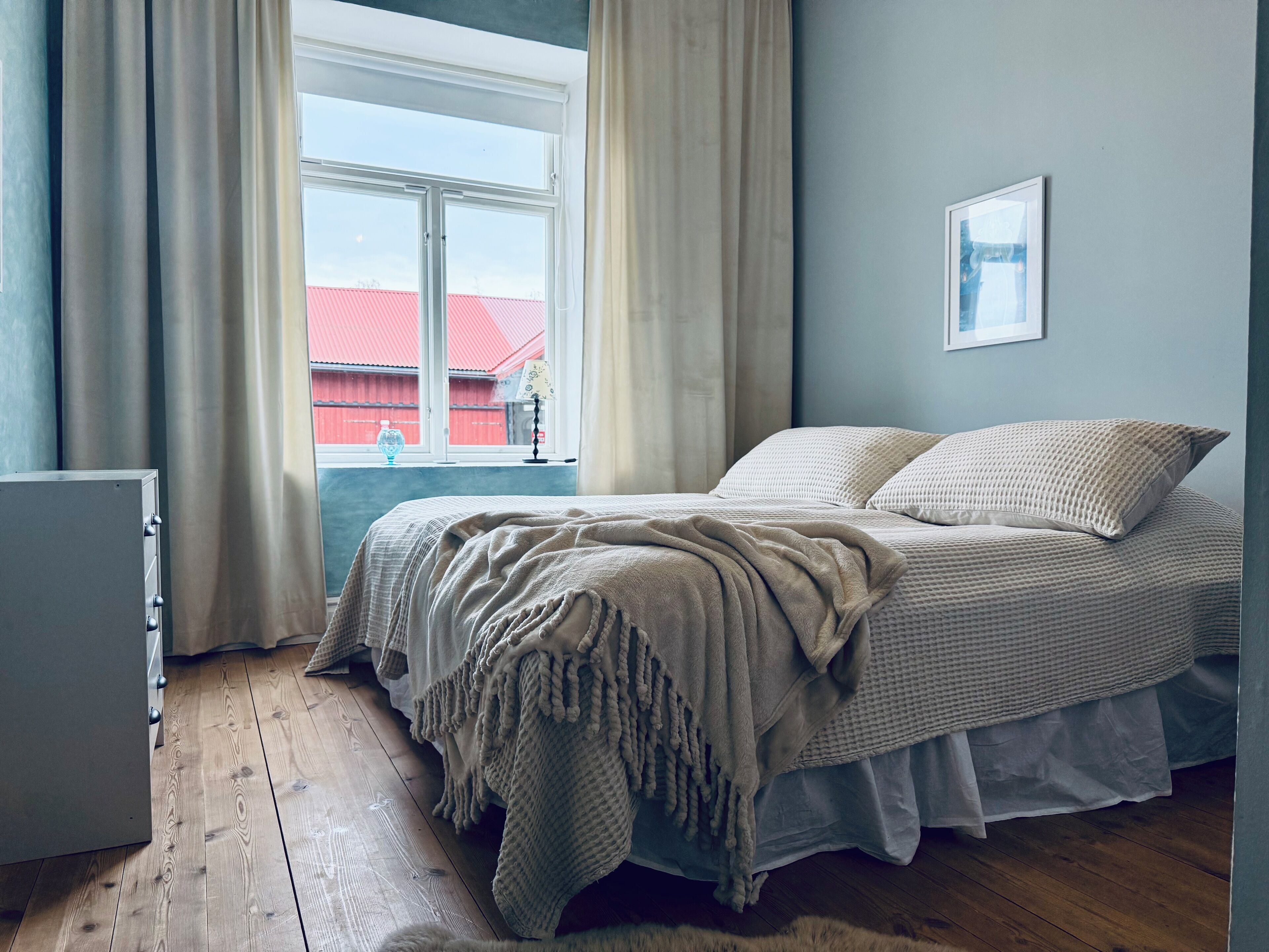Un dormitorio con cama, ventana, lámpara y un pequeño armario.