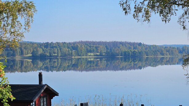 Un chalet au bord du lac, avec un quai, une chaise et une table.