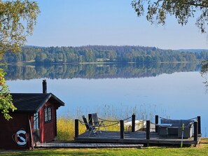 Una cabaña junto al lago con un muelle, una silla y una mesa.