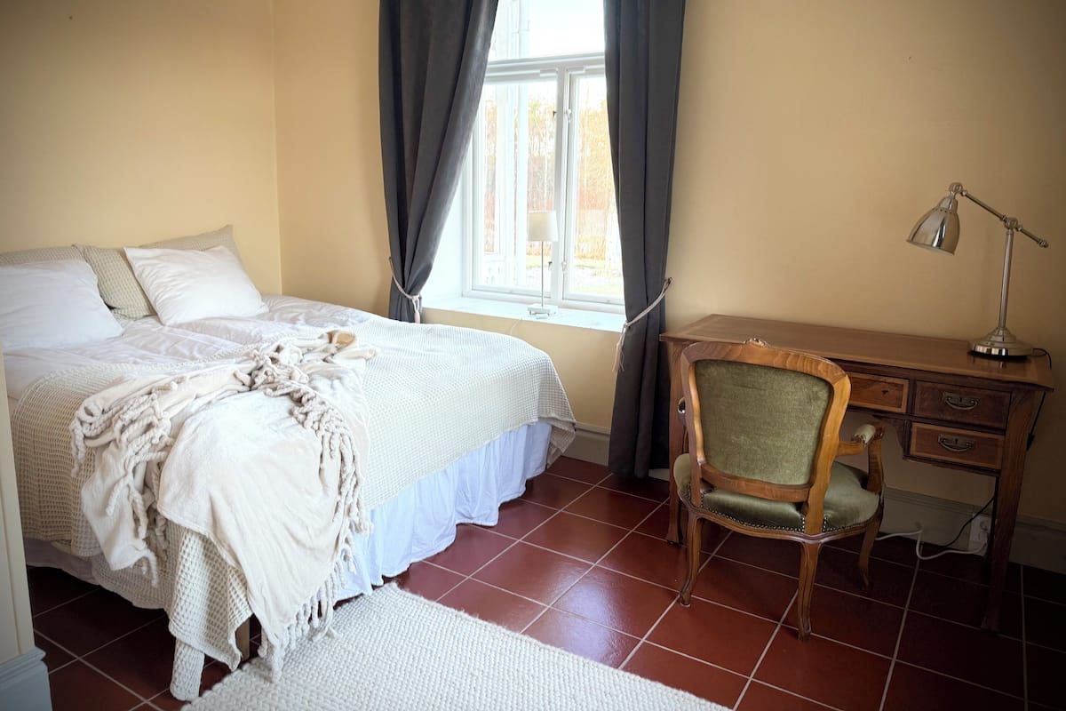 Un dormitorio con cama, escritorio, silla y ventana con cortinas.