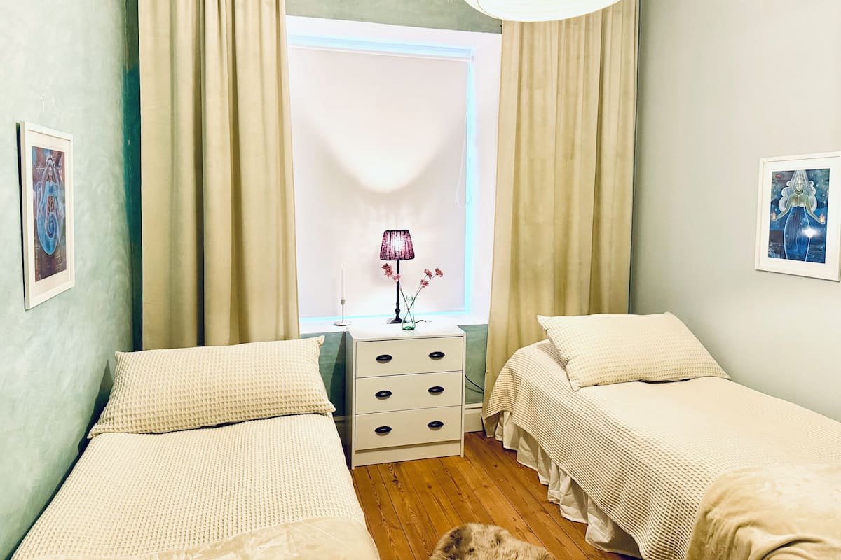Un dormitorio con dos camas, una mesita de noche, una lámpara y una ventana con cortinas.