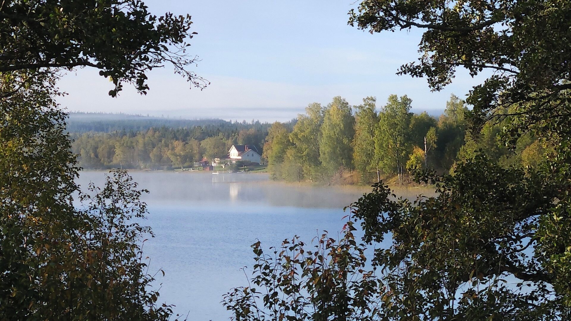 En sjö omgiven av träd, med ett hus som syns på avstånd.