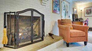 A living room with a fireplace, a cushioned armchair, and a painting on the wall.