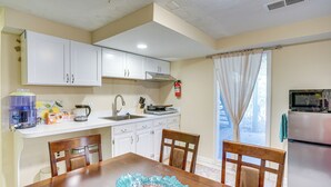 A kitchen with white cabinets, a sink, a stove, and a refrigerator. There is a dining table with chairs and a decorative glass bowl.