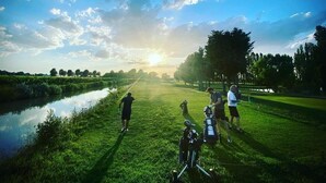 A golf course with a water body, trees, and people. - TENUTA SANTO STEFANO - HOTEL (Campagnola Emilia)