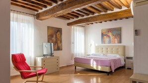 A bedroom with a bed, a red chair, a TV, and artwork on the walls. - TENUTA SANTO STEFANO - HOTEL (Campagnola Emilia)