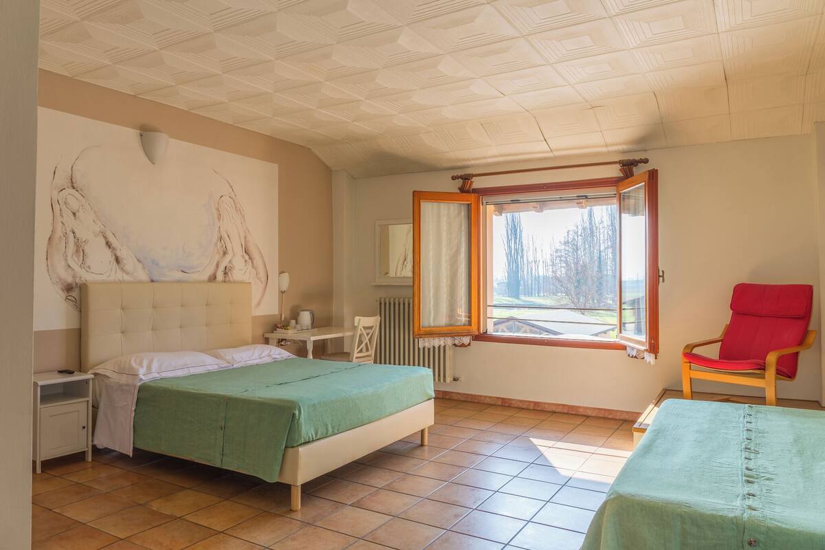 Et soveværelse med en seng, en stol, et natbord, et vindue og en radiator.