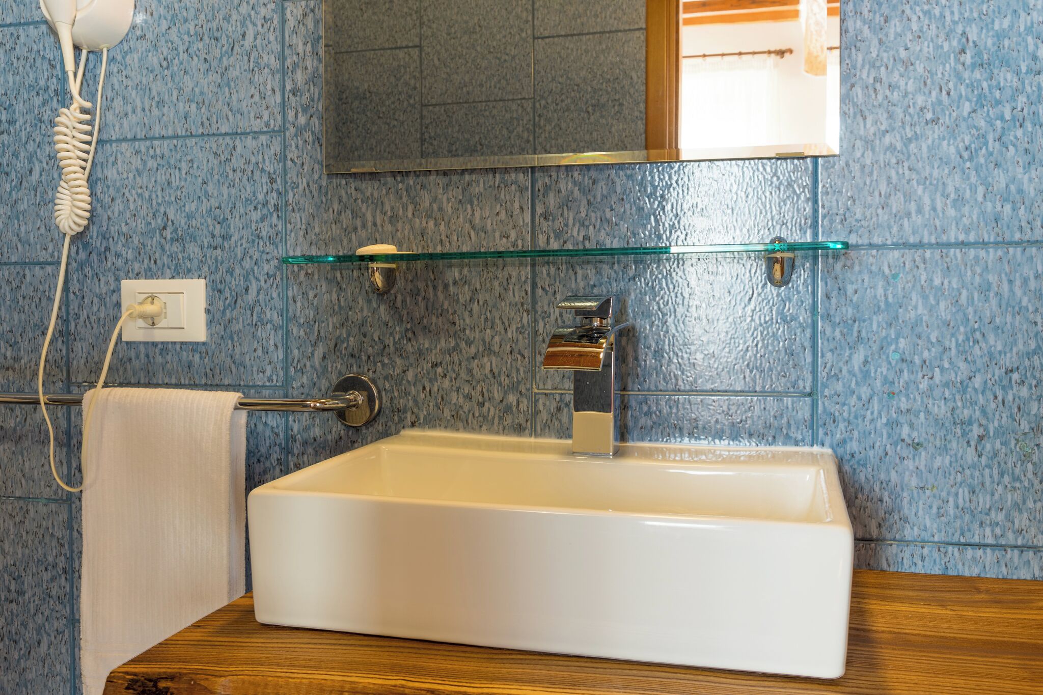A bathroom with a white sink, a glass shelf, a towel rack, and a telephone.