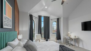 Quarto moderno com uma cama grande, duas cadeiras, uma escrivaninha e uma televisão.