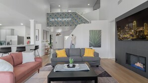 Uma sala de estar moderna com um sofá cinzento, um sofá rosa, uma mesa de centro preta com um tabuleiro e planta, uma lareira e uma escada com papel de parede floral.
