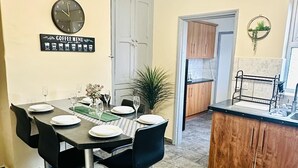 A dining area with a table set for four, a clock, and a coffee menu sign on the wall. - 3-bedroom St faith street Lincoln location+comfort+FREE parking for 2 cars (Lincoln)