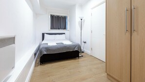 Un dormitorio pequeño y moderno con cama, armario y ventana con cortinas.