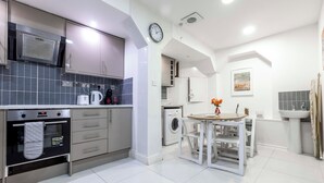 Una cocina moderna con horno empotrado, microondas y lavabo. Hay una zona de comedor con mesa y sillas, y una lavadora al fondo.