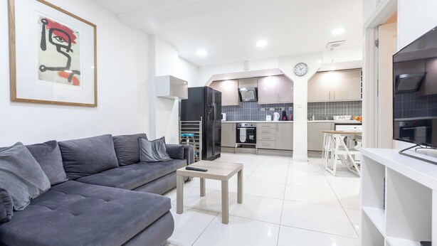 Una sala de estar moderna con un sofá gris, una pequeña mesa de centro de madera y una cocina al fondo.