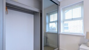 A room with a sliding glass door closet, a window with blinds, and a white bedside table. - Corner by the Canal - Leeds Central Duplex - Pass the Keys (Leeds)