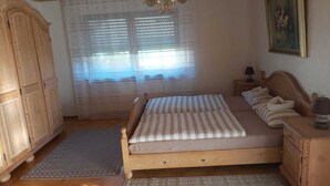 Une chambre à coucher avec un lit en bois, une table de chevet avec une lampe, une armoire et une fenêtre avec des stores.