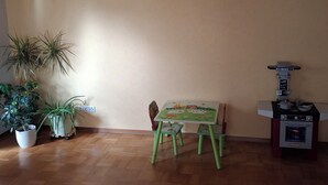 Une pièce avec un plancher en bois, une table verte avec des chaises, une plante en pot et un petit coin cuisine équipé d’un four à micro-ondes.