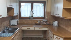 Une cuisine de taille réduite avec des meubles blancs, un four à micro-ondes, un évier et une fenêtre avec un rideau.