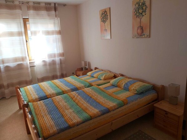 A bedroom with a wooden bed, striped bedding, a nightstand, a lamp, and two wall-mounted paintings. - Farm Vacations (Aspach)