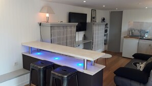 Eine moderne Küche mit Einbauofen, Mikrowelle und Kaffeemaschine. Es gibt eine Bar mit Hockern und blauer Beleuchtung unter den Schränken.