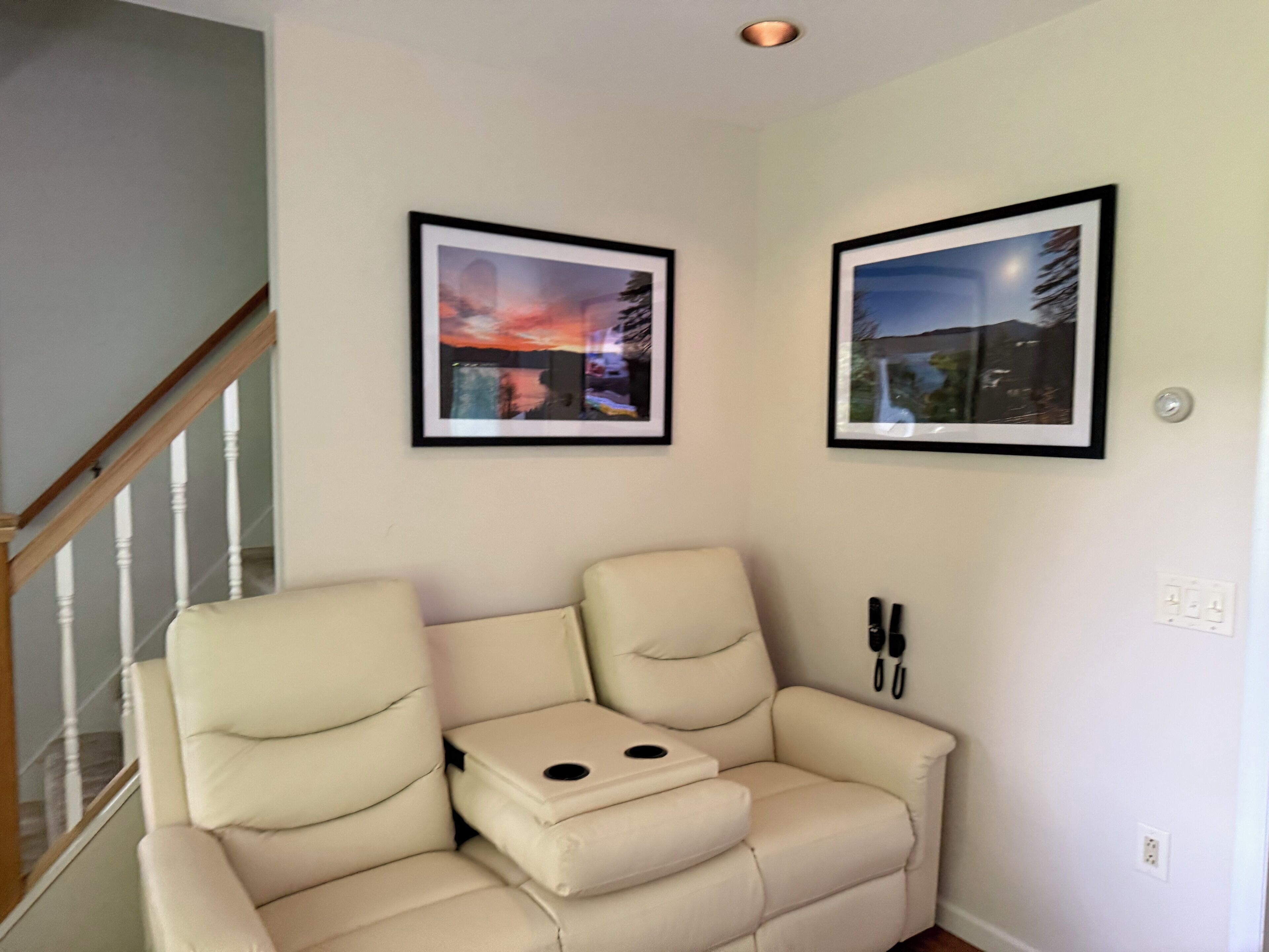 Un salon avec un canapé beige, une petite table et deux tableaux encadrés accrochés au mur.
