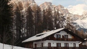 A chalet-style building with a balcony, surrounded by snow-covered mountains and trees. - Cozy apartment with beautiful view of the Olympic Cortina d' Ampezzo (Cortina d'Ampezzo)