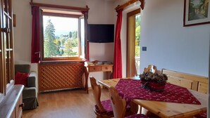 A cozy room with a wooden table and chairs, a window with red curtains, and a view of greenery outside. - Cozy apartment with beautiful view of the Olympic Cortina d' Ampezzo (Cortina d'Ampezzo)
