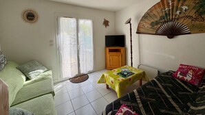 A living room with a sofa, a table with a book, a TV, and a decorative fan. - Charming holiday home 400m from the beach (Saint-Hilaire-de-Riez)