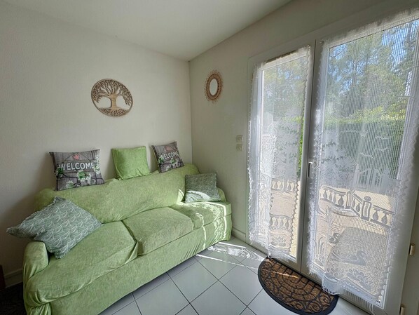 A green sofa with patterned cushions, a welcome sign, and a decorative wreath on the wall.