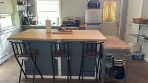 Een keuken met een centraal eiland, barstoelen, een magnetron, een koelkast en een klok aan de muur.