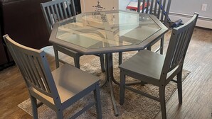Een eetgedeelte met een tafel met glazen blad, omringd door zes stoelen, een witte kast met Heritage logo en een raam met jaloezieën.