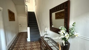 Un pasillo con suelo estampado, una escalera, una consola con espejo y una puerta.