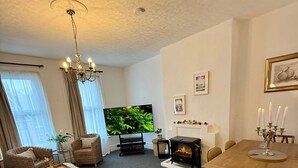 Una sala de estar con sofá, televisor, chimenea, mesa de comedor y candelabro.
