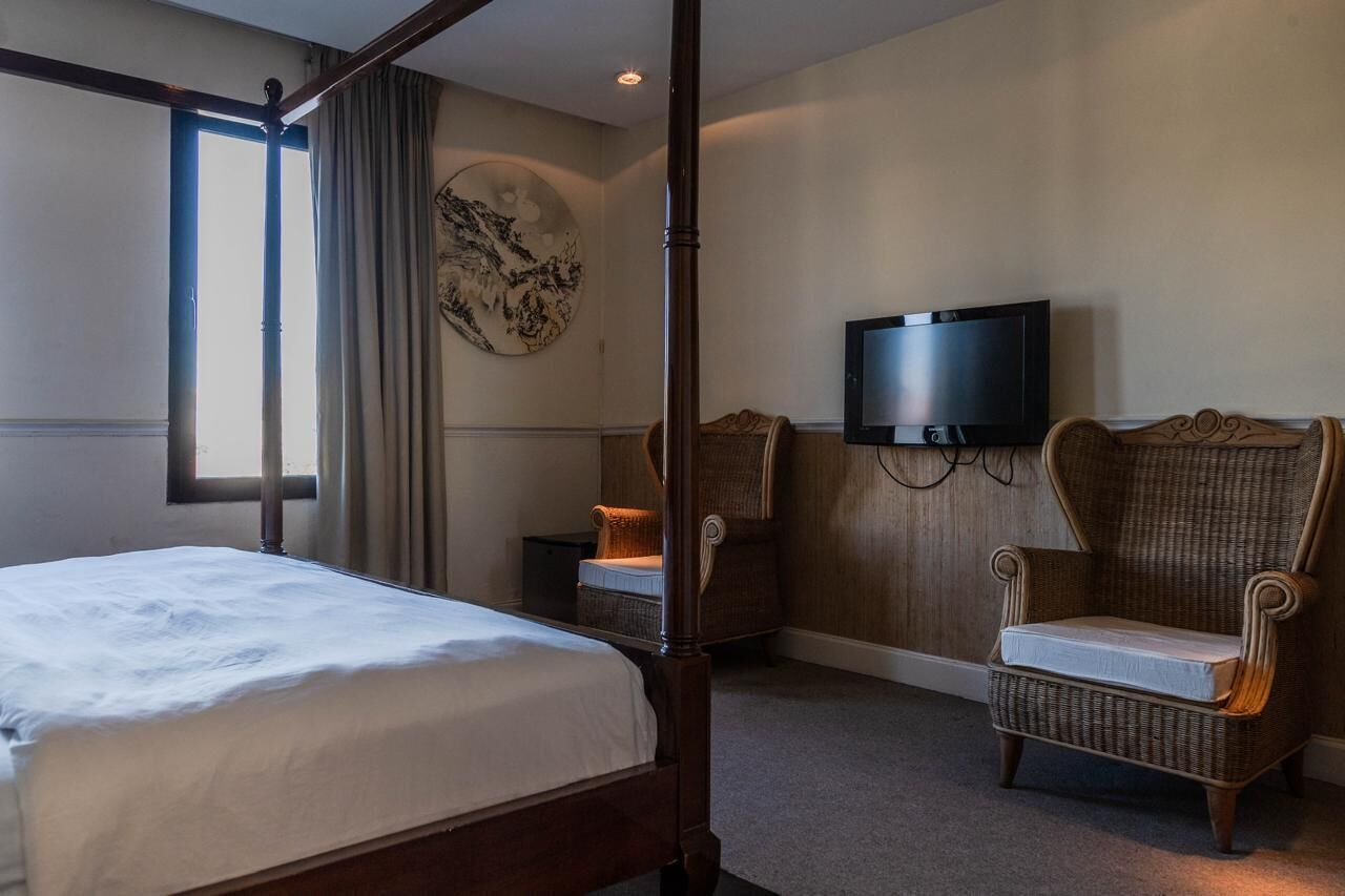 Una cama con dosel, un televisor, una silla de mimbre y una obra de arte colgada en la pared en una habitación de hotel.