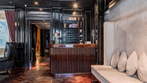 Una hall d'albergo con una reception, una zona salotto con un divano, una libreria e un pavimento a motivi a spina di pesce.