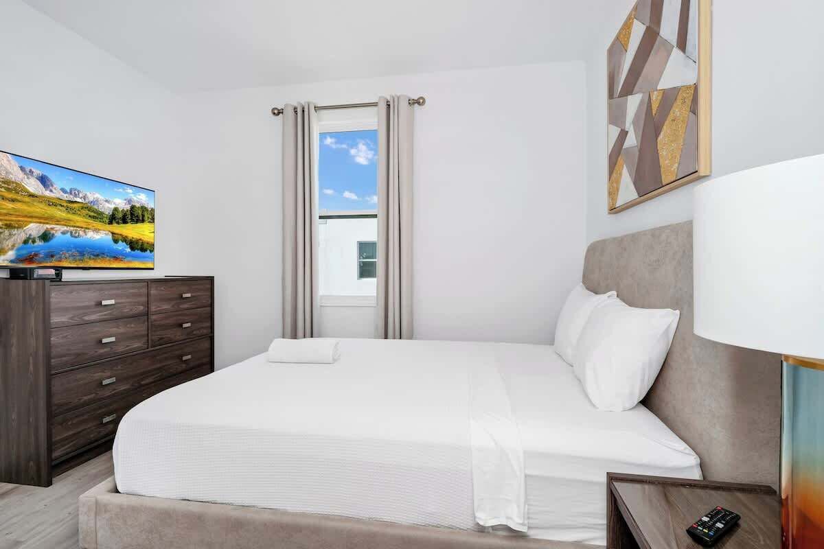 Une chambre d’hôtel moderne avec un grand lit, une commode, un téléviseur sur le côté gauche et une fenêtre avec des rideaux.