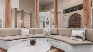 A modern living room with a curved sectional sofa, a round coffee table, and large wooden beams. - Relaxing 3BR Haven w/ Pool & BBQ for Family Time (Mesa)