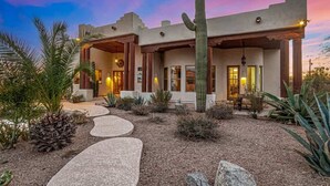 A desert-style building with a large cactus in the front, a stone pathway leading to the entrance, and a warm interior glow. - Relaxing 3BR Haven w/ Pool & BBQ for Family Time (Mesa)