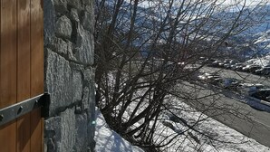 Un muro de piedra con una puerta de madera, vista a un paisaje nevado y cielo despejado.