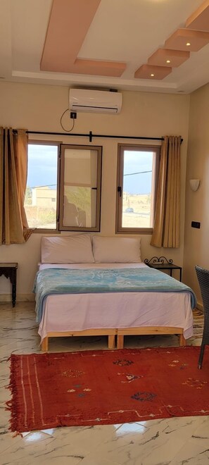 A bedroom with a bed, a window, a red rug, and a chair. - Auberge Famille BenMoro (Skoura)