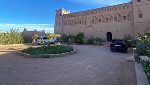 A large, historic building with a central courtyard, a paved driveway, and a parked car. - Auberge Famille BenMoro (Skoura)