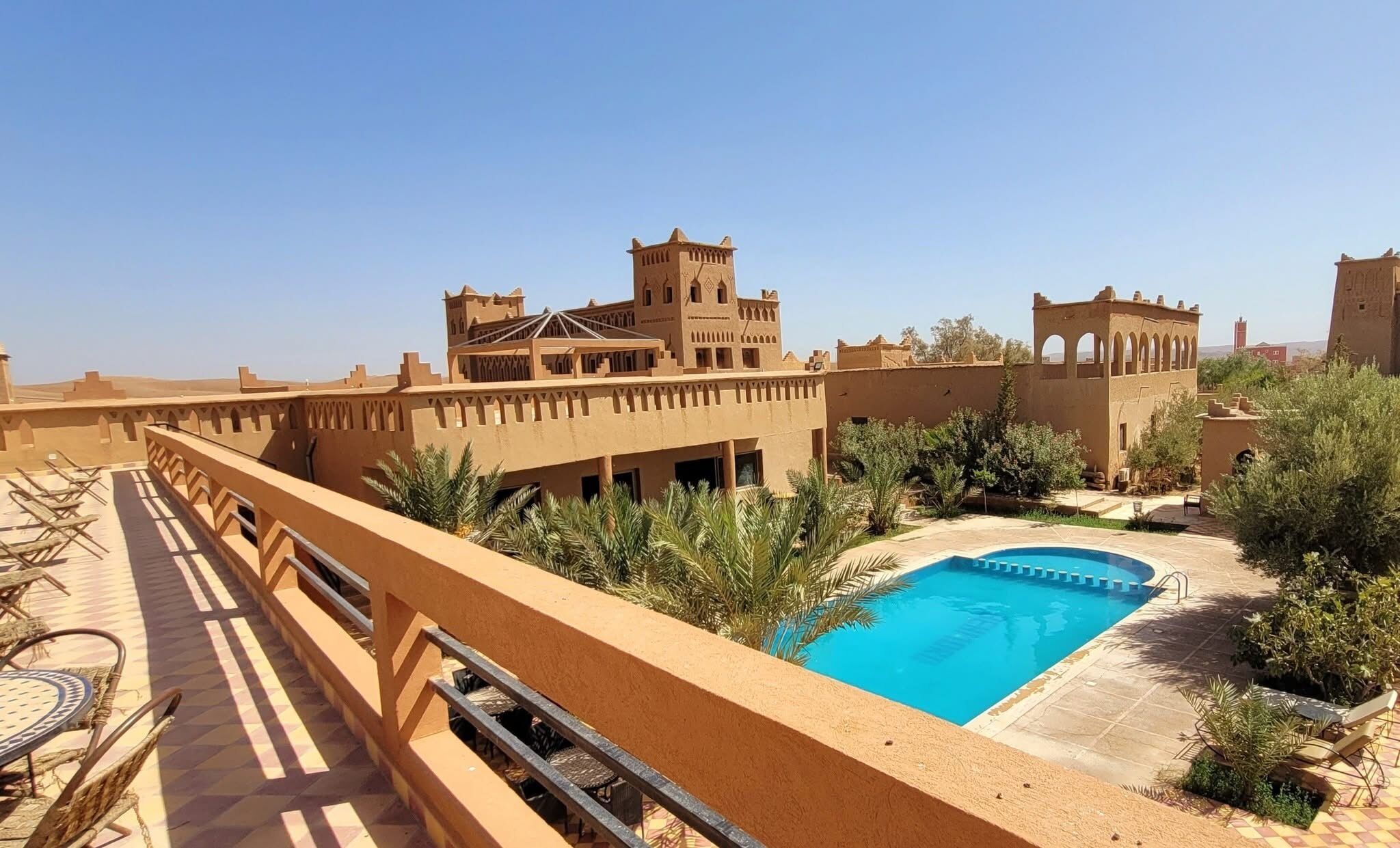 Un espace piscine avec une eau d’un bleu limpide, entouré de palmiers et bordé d’un bâtiment à l’architecture traditionnelle.