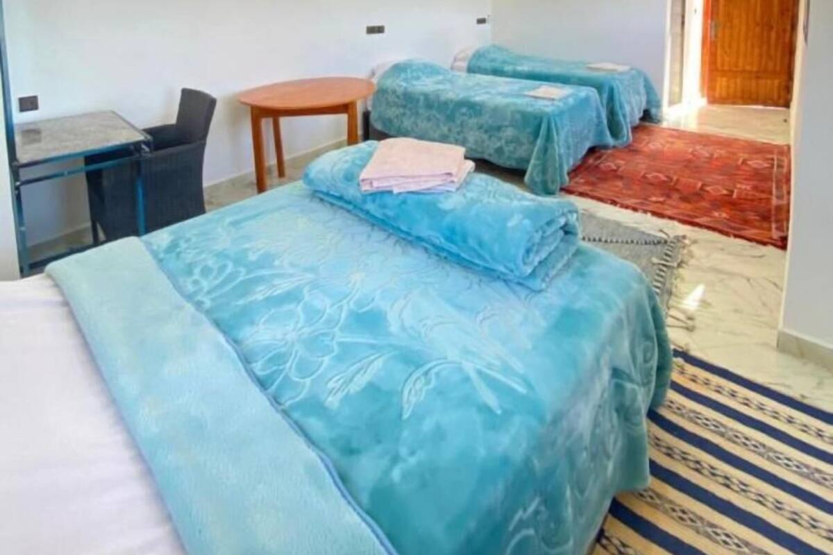 A hotel room with two beds, a desk, a chair, and a small table.