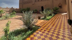A courtyard with a checkered floor leading to a building with arched windows and a tower. - Auberge Famille BenMoro (Skoura)