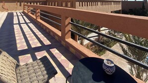 A rooftop terrace with a tiled floor, a woven chair, and a decorative pot. - Auberge Famille BenMoro (Skoura)