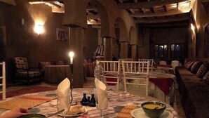 A dimly lit dining area with rustic wooden furniture, a patterned tablecloth, and candlelight. - Auberge Famille BenMoro (Skoura)