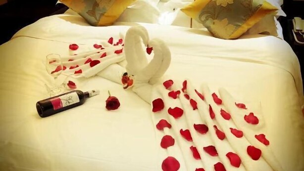 A bed with rose petals and a swan-shaped arrangement of towels. - Huaxia Jingdu Business Hotel (Taiyuan)