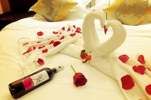 Un lit décoré d’une serviette en forme de cygne, de pétales de rose, d’une bouteille de vin et de verres.