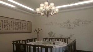 A dining area with a round table, chairs, and a chandelier. There is a large framed artwork on the wall and a smaller painting depicting a landscape. - Huaxia Jingdu Business Hotel (Taiyuan)